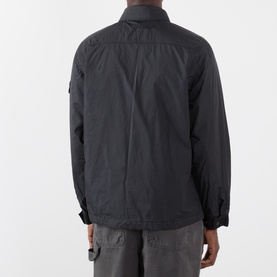 Model wearing Stone Island black casual jacket, rear view, showing badge patch on sleeve and cargo trousers styled beneath.
