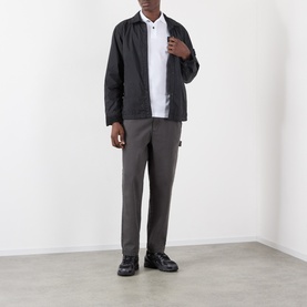 Model wearing Stone Island black casual jacket in polyamide, styled with white polo shirt, grey trousers and black shoes.