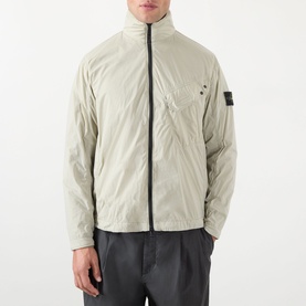 Model wearing Stone Island Compass Logo Ultralight Windbreaker in sand, with funnel neck, chest pocket, and two-way zip, styled with dark trousers.
