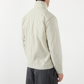 Model wearing Stone Island Compass Logo Ultralight Windbreaker in sand, rear view, styled with grey trousers. Lightweight nylon jacket with funnel