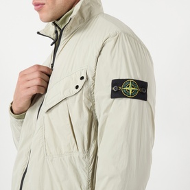 Model wearing Stone Island Compass Logo Ultralight Windbreaker in sand, showing sleeve badge and chest pocket detail with zip fastening
