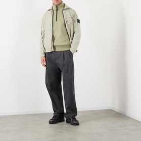 Model wearing Stone Island Compass Logo Ultralight Windbreaker in sand over a hoodie, with dark charcoal trousers and black trainers.