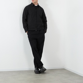 Model wearing Stone Island black cotton casual shirt with matching black trousers and dark trainers.
