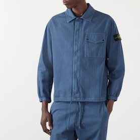Model wearing Stone Island Blu Ardesia cotton casual shirt with ribbed texture, chest pocket, and badge logo, styled with matching trousers.