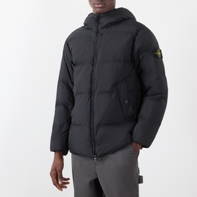 Model wearing Stone Island black hooded puffer jacket with signature compass badge patch, styled with grey trousers.