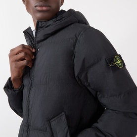 Model wearing Stone Island black hooded puffer jacket, close-up showing compass badge patch on sleeve and zip fastening
