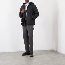 Model wearing Stone Island black casual jacket with hood, styled with grey trousers, white polo shirt and black crossbody bag.