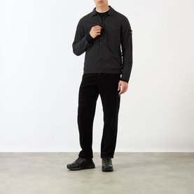 Model wearing Stone Island Logo Badge Zip Overshirt in black with black trousers and dark trainers.
