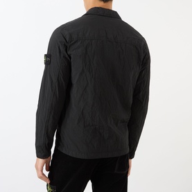Model wearing Stone Island Logo Badge Zip Overshirt in black, rear view, showing logo badge on sleeve and crinkled nylon finish.