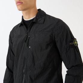 Model wearing Stone Island Logo Badge Zip Overshirt in black, showing logo badge on sleeve, zip fastening and chest pocket, styled over dark crew