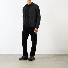 Model wearing Stone Island Logo Badge Zip Overshirt in black, styled with black trousers and black trainers.