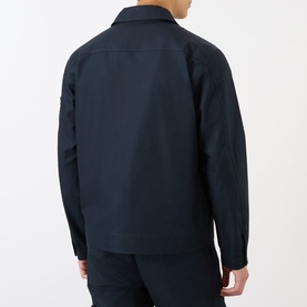 Model wearing Stone Island Tonal Logo Badge Zip Overshirt in blue, rear view, point collar, smooth cotton finish, styled with navy trousers