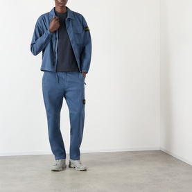 Model wearing Stone Island BLU ARDESIA casual trousers, styled with matching blue overshirt and grey trainers.