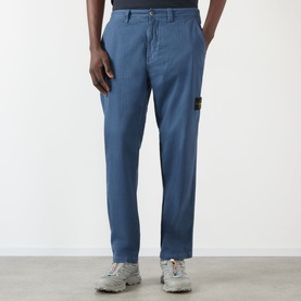 Model wearing Stone Island Blu Ardesia casual trousers with signature compass badge patch, paired with white chunky trainers.