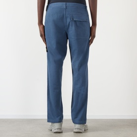 Model wearing Stone Island BLU ARDESIA casual trousers, rear view, with chest pocket detail, paired with grey trainers.