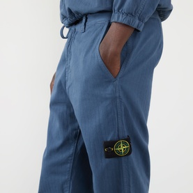Model wearing Stone Island Blu Ardesia casual trousers, cotton blend with signature compass badge patch, hands in pockets, paired with matching