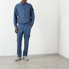Model wearing Stone Island Blu Ardesia casual trousers with matching overshirt and grey trainers.