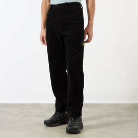 Model wearing Stone Island Logo Badge Corduroy Trousers in black, straight-leg fit with logo badge detail, styled with dark trainers.