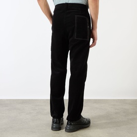 Model wearing Stone Island Logo Badge Corduroy Trousers in black, straight-leg fit with contrasting rear pocket detail, styled with black trainers.