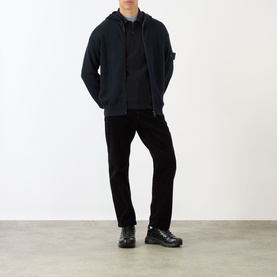 Model wearing Stone Island Logo Badge Corduroy Trousers in black, styled with a navy zip-up hoodie and dark chunky-sole boots.