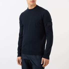 Model wearing Stone Island blue virgin wool crew neck jumper with signature sleeve badge, styled with navy trousers.