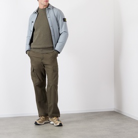 Model wearing Stone Island Verde Militare Melange wool crew neck, styled with light blue overshirt, olive cargo trousers and tan trainers.