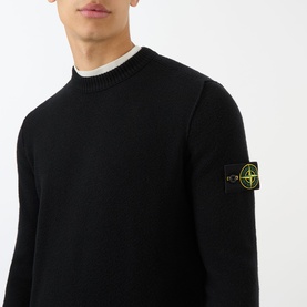 Model wearing Stone Island black crew neck knit sweater with signature compass badge on left sleeve, styled with white crew neck underneath