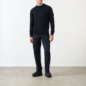 Model wearing Stone Island blue cotton chino trousers, styled with a navy crewneck knit and black chunky trainers.