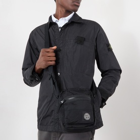 Model carrying Stone Island black nylon crossbody bag with logo patch, worn across chest, styled with matching black overshirt jacket