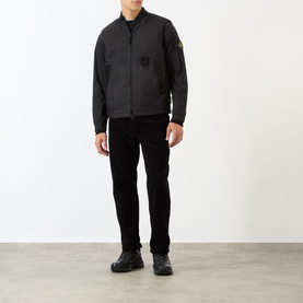 Model wearing Stone Island black Logo Badge Gilet over long-sleeve top, styled with black cord trousers and chunky black trainers.