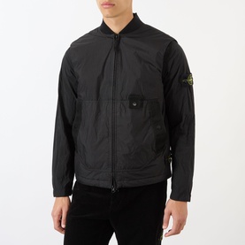 Model wearing Stone Island Logo Badge Gilet in black, featuring bomber collar, two-way zip, snap-button chest pocket and logo badge detail.