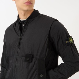 Model wearing Stone Island Logo Badge Gilet in black, sleeveless with bomber collar, logo badge on sleeve, layered over long-sleeve top