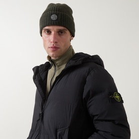 Model with Stone Island military green wool ribbed beanie hat featuring logo badge, styled with black padded jacket