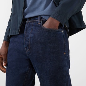 Model wearing Stone Island blue rinse jeans, styled with a teal shirt and jacket, hand in pocket, close-up torso shot.