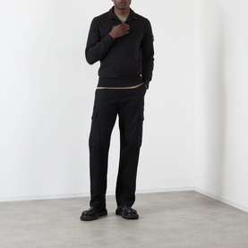 Model wearing Stone Island black cotton polo with zip collar, styled with black cargo trousers and black leather shoes.