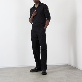 Model wearing Stone Island black cotton polo with half-zip, styled with matching black cargo trousers and black boots