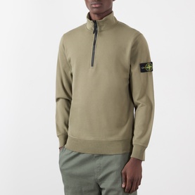 Model wearing Stone Island military green cotton half-zip sweatshirt with ribbed cuffs, hem, and signature arm badge patch