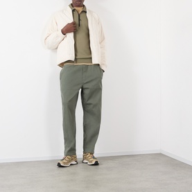 Model wearing Stone Island military green cotton polo, styled with cream padded jacket, olive trousers, and gold trainers.