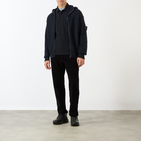 Model wearing Stone Island Compass Logo Long-Sleeved Polo Shirt in blue, styled with navy zip hoodie and black trousers.