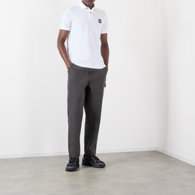 Model wearing Stone Island white polo shirt with chest badge logo, styled with grey trousers and black shoes