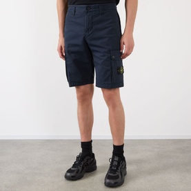 Model wearing Stone Island Compass Logo Bermuda Shorts in navy blue with cargo pockets and logo badge, styled with black trainers and socks.