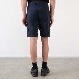 Model wearing Stone Island Compass Logo Bermuda Shorts in navy blue, featuring cargo pockets. Styled with black socks and trainers.