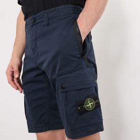 Model wearing Stone Island Compass Logo Bermuda Shorts in navy blue, with cargo pocket and green compass badge badge detail visible.