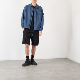 Model wearing Stone Island black cotton cargo shorts with multiple pockets, styled with a blue zip overshirt and black trainers.