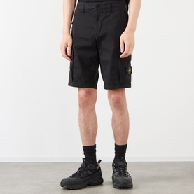 Model wearing Stone Island black cotton cargo shorts with signature compass badge patch on left thigh, styled with black trainers.