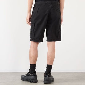 Model wearing Stone Island black cotton cargo shorts, rear view, styled with black socks and chunky trainers.