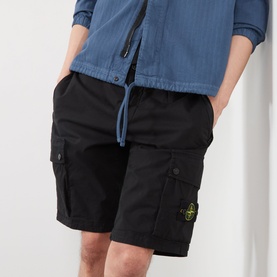 Model wearing Stone Island black cotton cargo shorts with drawstring waist, multiple pockets and logo badge, styled with a blue shirt.