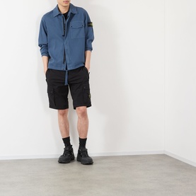 Model wearing Stone Island black cotton cargo shorts with zip pockets, styled with a blue overshirt and black boots.