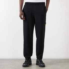 Model wearing Stone Island black cotton sweatpants with compass badge patch on left leg, styled with black chunky sole trainers