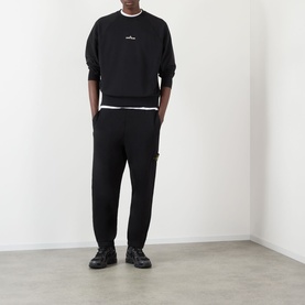 Model wearing Stone Island black cotton sweatpants, styled with matching black sweatshirt and black trainers.